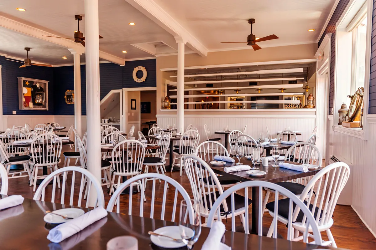 A comfortable and welcoming dining area featuring wooden tables and white chairs, complemented by a bar area and decorative wall art. The room is set up for socializing and casual gatherings, with a relaxed atmosphere ideal for families enjoying meals together.