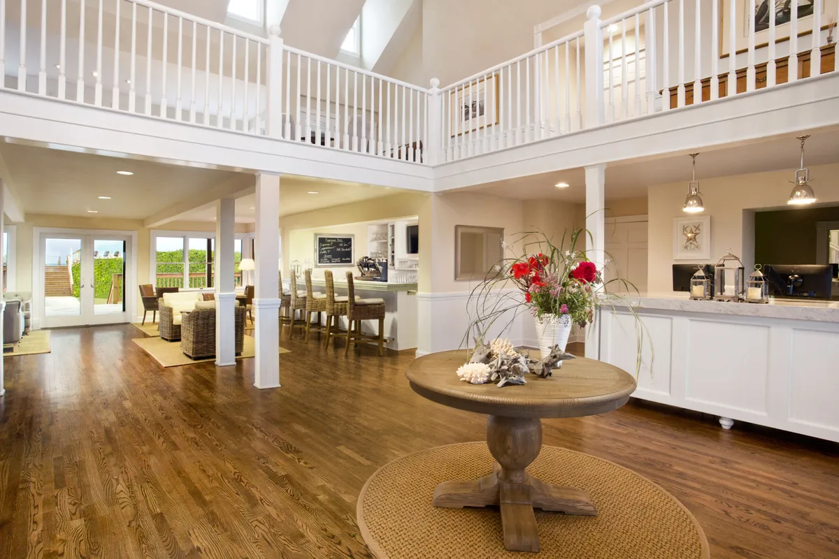 A spacious, sunlit interior featuring a central round table adorned with fresh flowers, an open kitchen, and a large dining area with ample seating. The setting is warm and inviting, ideal for group gatherings or relaxed meals.