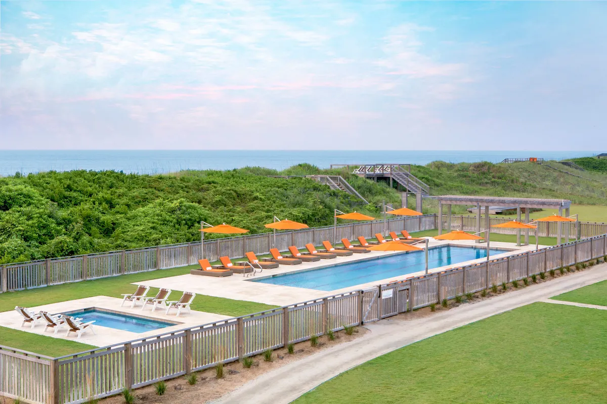 This image features a swimming pool area with inviting lounge chairs and orange umbrellas. In the background, you can see balconies with ocean views, and the landscape transitions toward the water. The perspective conveys both the resort’s leisure amenities and the direct relationship between the balcony spaces and the Atlantic vistas.